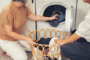 Senior couple working together to complete their household chores at the washing machine in a happy and contented manner. Husband and wife doing the usual tasks in the house. image